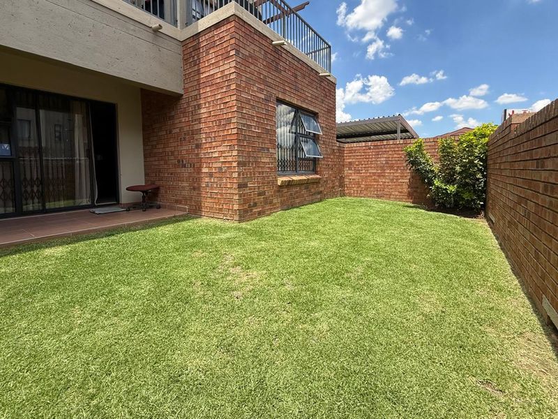 A private rear garden featuring a well-maintained lawn, brick boundary walls, and a paved patio area accessible via sliding glass doors.