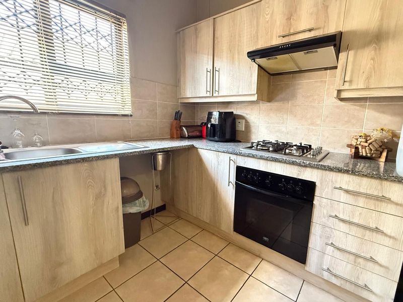 Functional kitchen featuring light wood-look cabinetry, granite-style countertops, built-in gas hob, oven, extractor fan, and tiled flooring with a window for natural light.