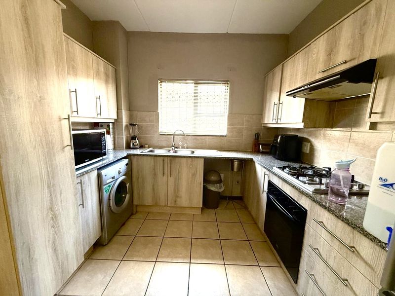 Functional kitchen featuring light wood-look cabinetry, granite countertops, built-in oven, gas hob, extractor fan, and integrated laundry plumbing.