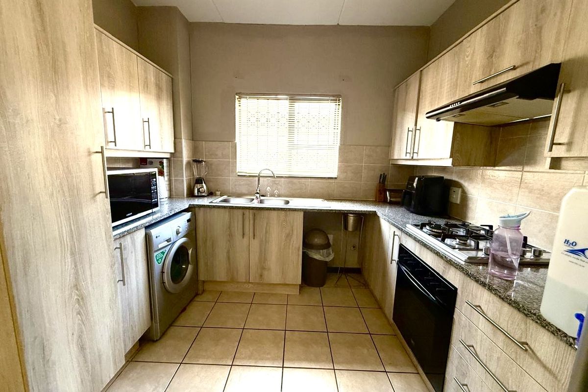 Functional kitchen featuring light wood-look cabinetry, granite countertops, built-in oven, gas hob, extractor fan, and integrated laundry plumbing.