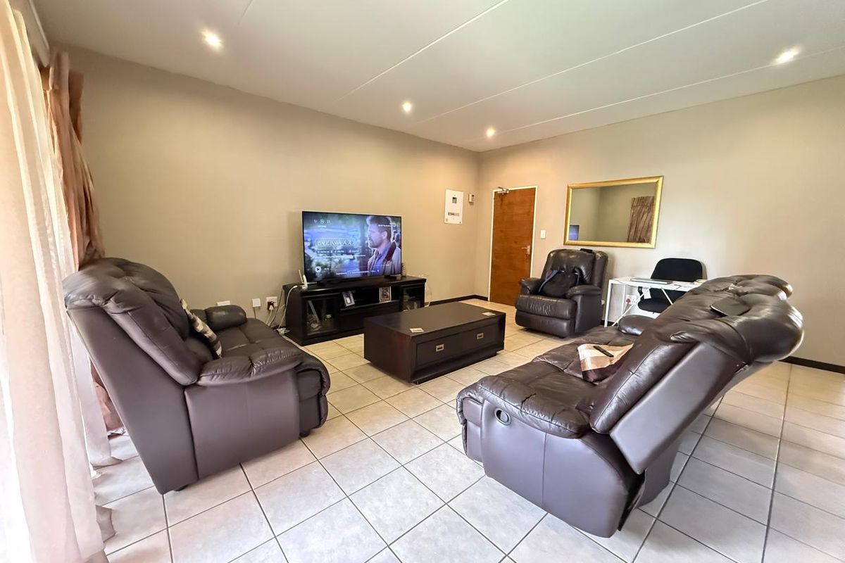 A spacious living room featuring neutral wall tones, tiled flooring, and recessed downlighting, providing a comfortable and functional area for relaxation.