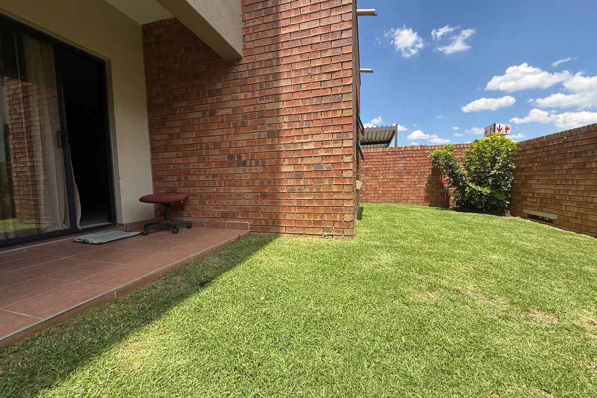 A private rear garden featuring a paved patio area, brick boundary walls, and a well-maintained lawn accessible via sliding glass doors.