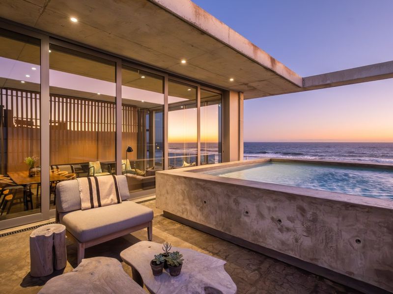 Modern outdoor patio area featuring a built-in concrete pool, recessed lighting, and expansive sliding glass doors with direct ocean views.
