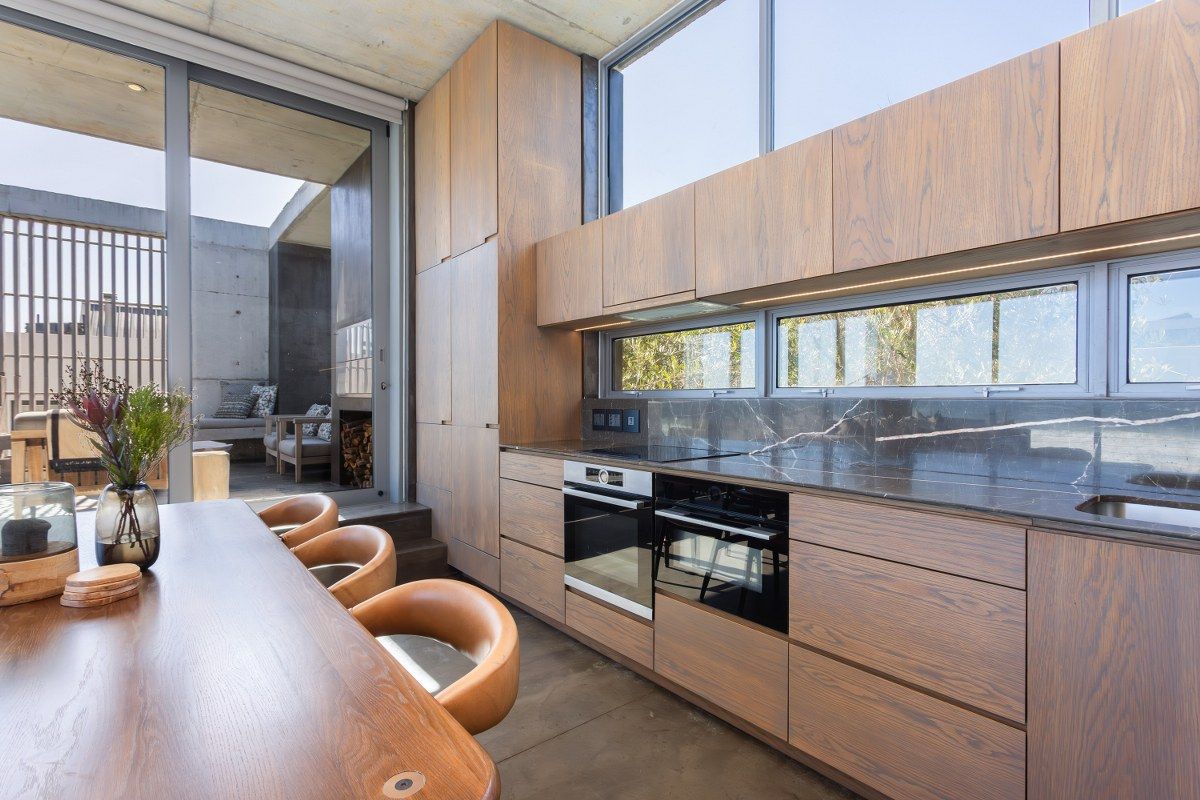 Modern kitchen featuring high-end wood cabinetry, stone countertops, integrated appliances, and seamless flow to an outdoor patio area.