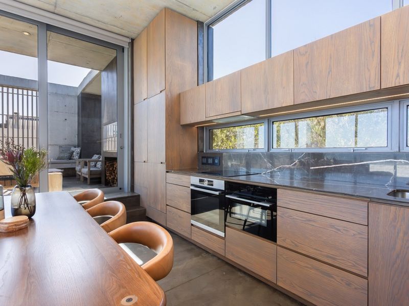 Modern kitchen featuring high-end wood cabinetry, stone countertops, integrated appliances, and seamless flow to an outdoor patio area.