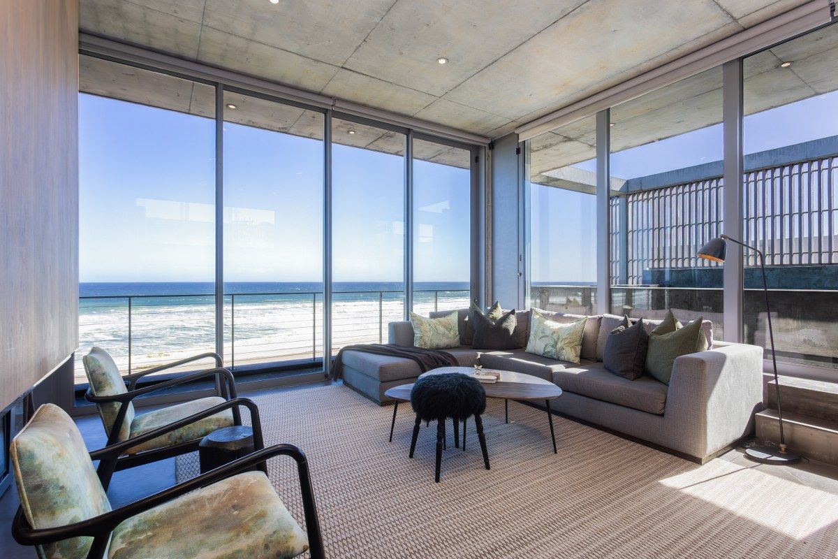 Modern living room featuring an exposed concrete ceiling, floor-to-ceiling glass walls, and expansive ocean views.