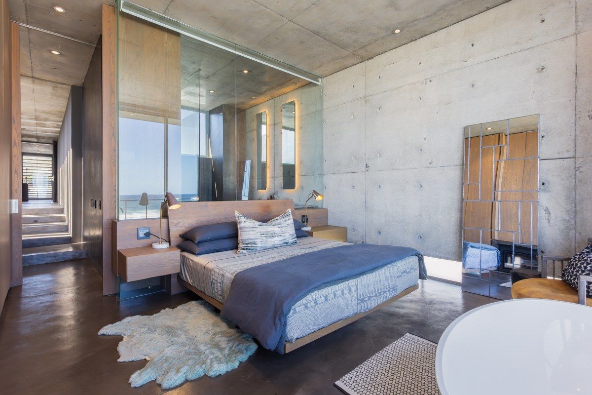 Modern bedroom featuring exposed concrete walls and ceiling, polished concrete floors, and a sleek glass partition wall with integrated lighting.