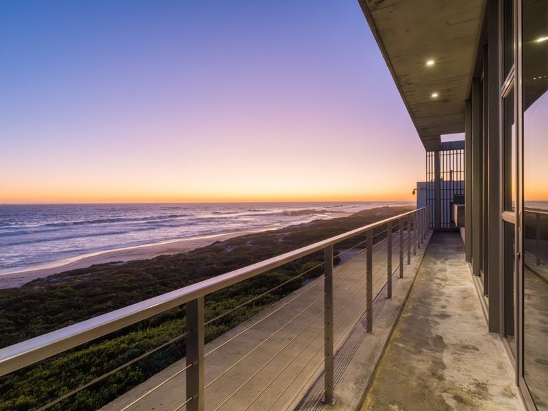 A spacious balcony featuring a metal railing and concrete flooring, offering expansive ocean views at sunset.