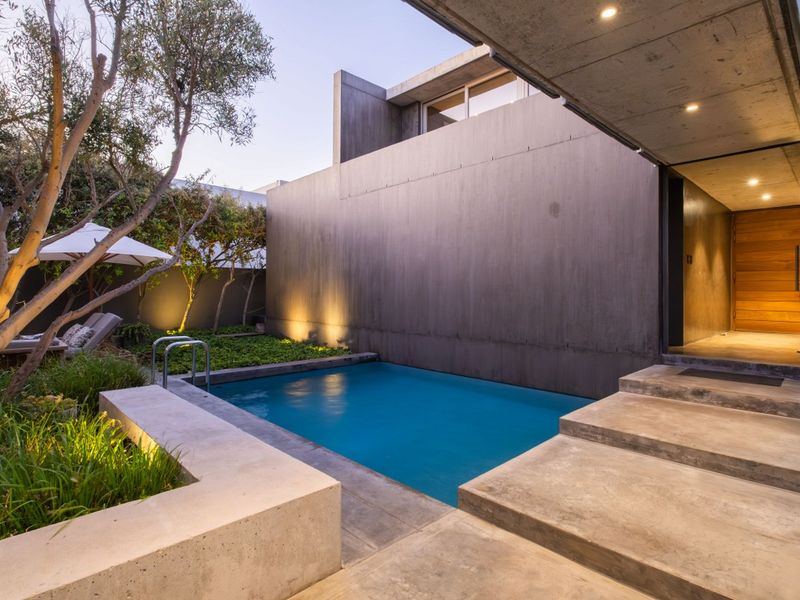 Modern architectural pool area featuring concrete construction, integrated lighting, and landscaped garden surroundings, creating a seamless indoor-outdoor transition.