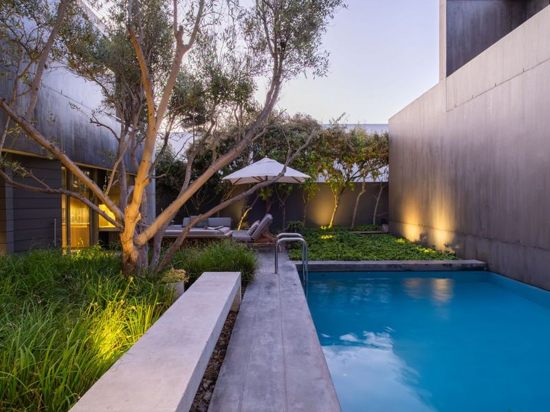 A modern, well-maintained courtyard featuring a swimming pool, integrated concrete bench seating, and professional landscape lighting.
