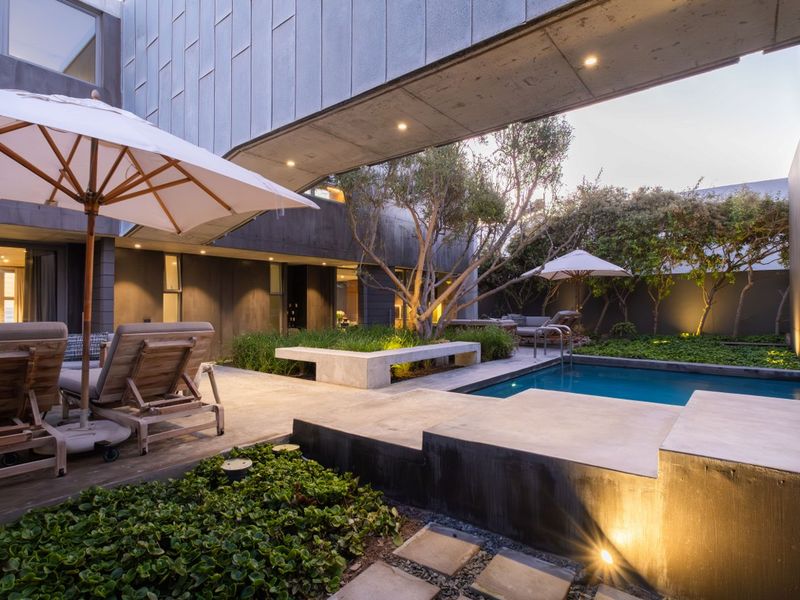 Modern courtyard featuring a swimming pool, integrated concrete bench, and landscaped garden, framed by contemporary architectural concrete walls and recessed lighting.