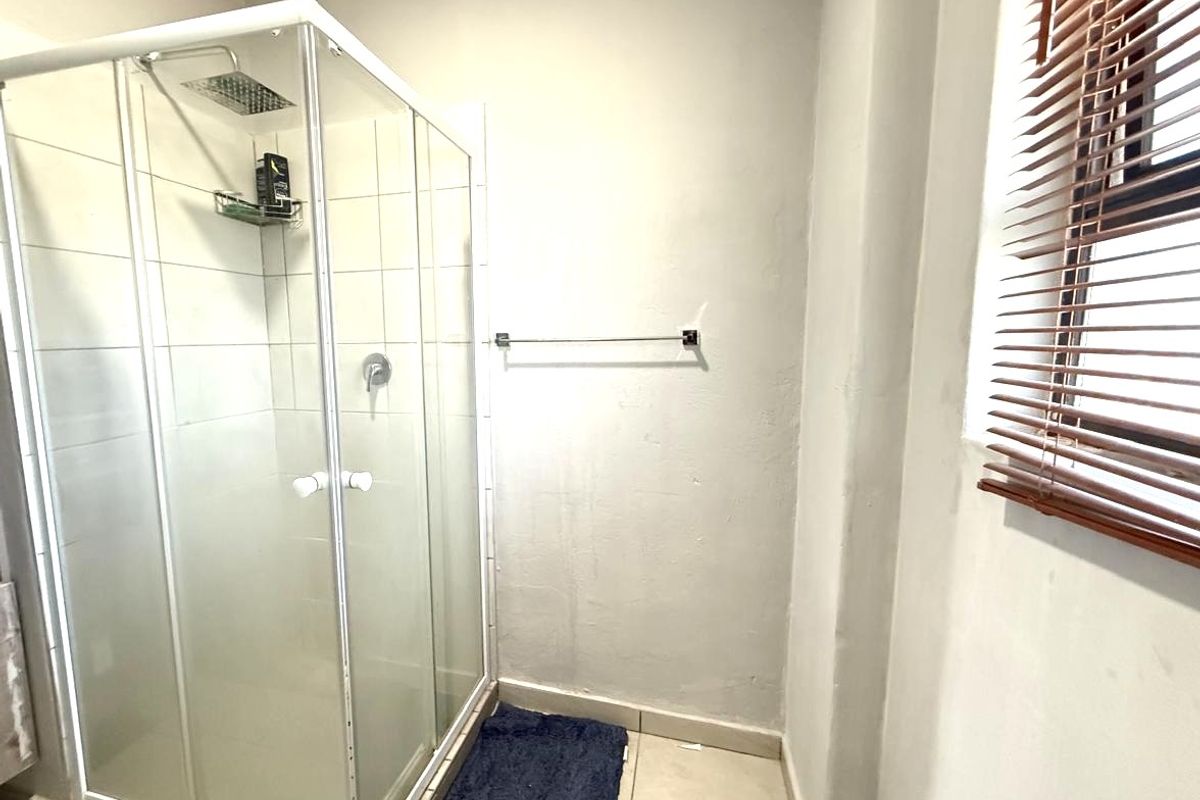 A functional bathroom featuring a glass-enclosed shower stall, tiled flooring, and a window fitted with wooden blinds.