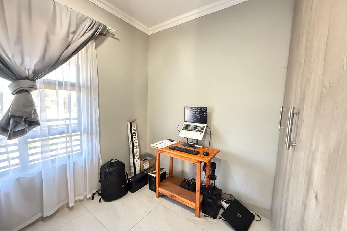 A compact bedroom featuring tiled flooring, built-in cabinetry, and a window with curtain treatments, suitable for use as a home office or guest room.