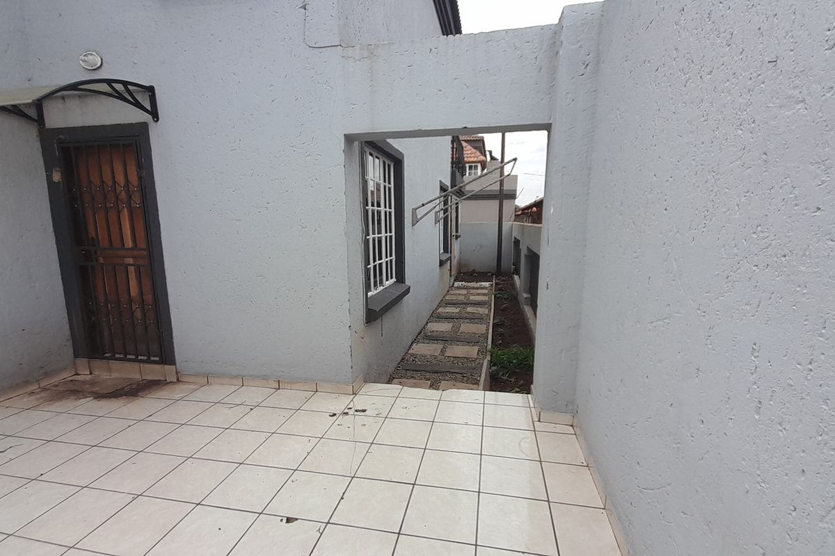 A rear exterior area featuring a tiled patio, security gate, and a paved walkway leading along the side of the townhouse.