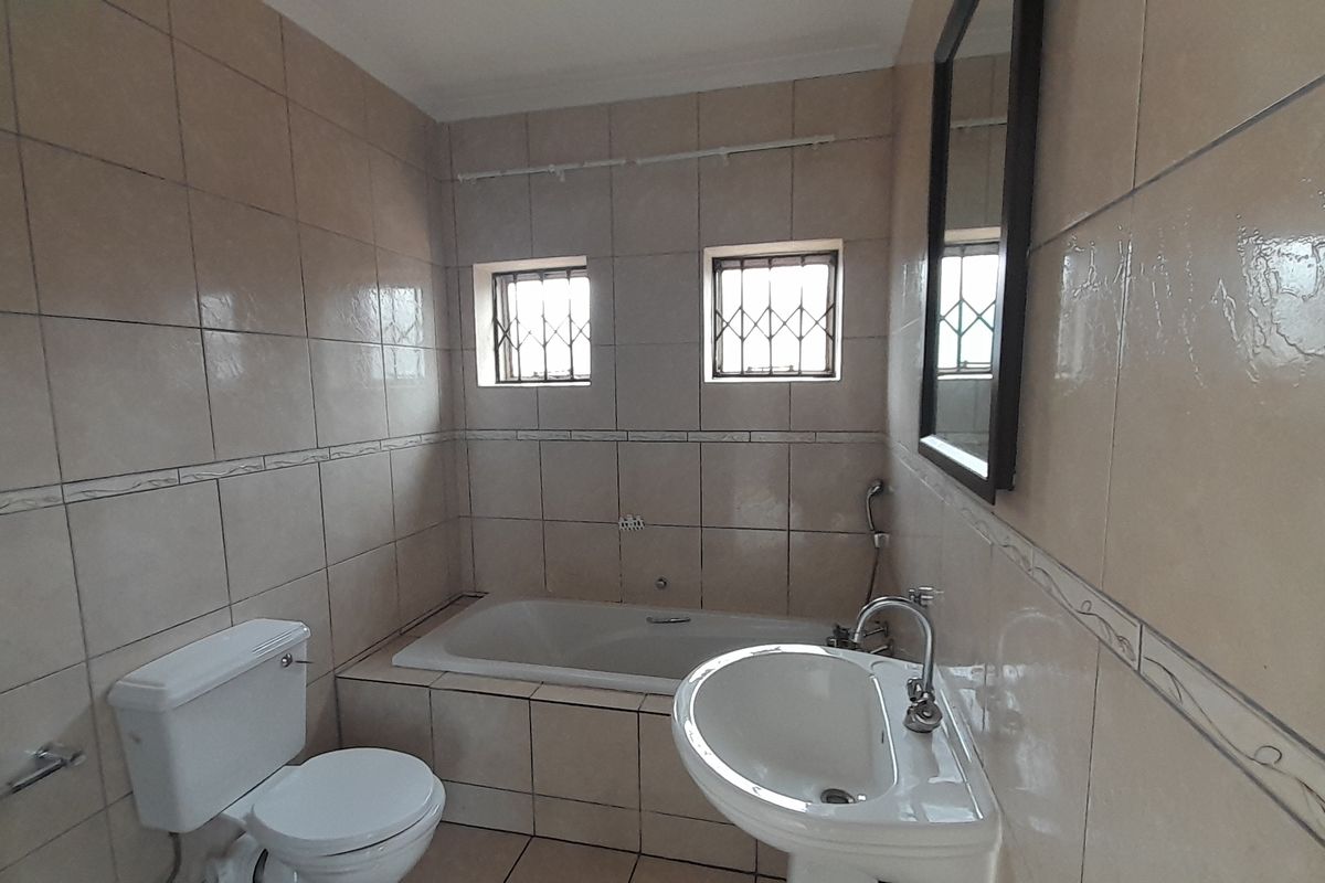 A functional bathroom featuring a built-in bathtub, pedestal basin, toilet, and neutral wall tiling with security bars on the windows.