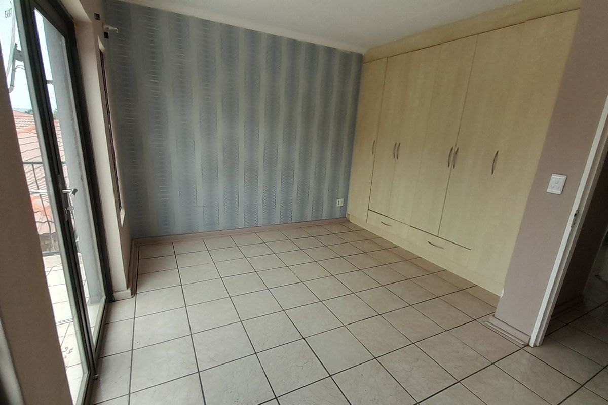 A bright, empty bedroom featuring built-in cupboards, tiled flooring, and a sliding glass door providing access to an outdoor area.
