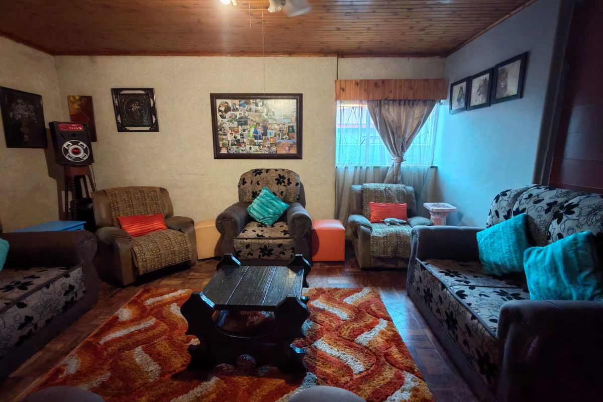 A living room featuring a timber ceiling and parquet flooring, with burglar bars on the window.