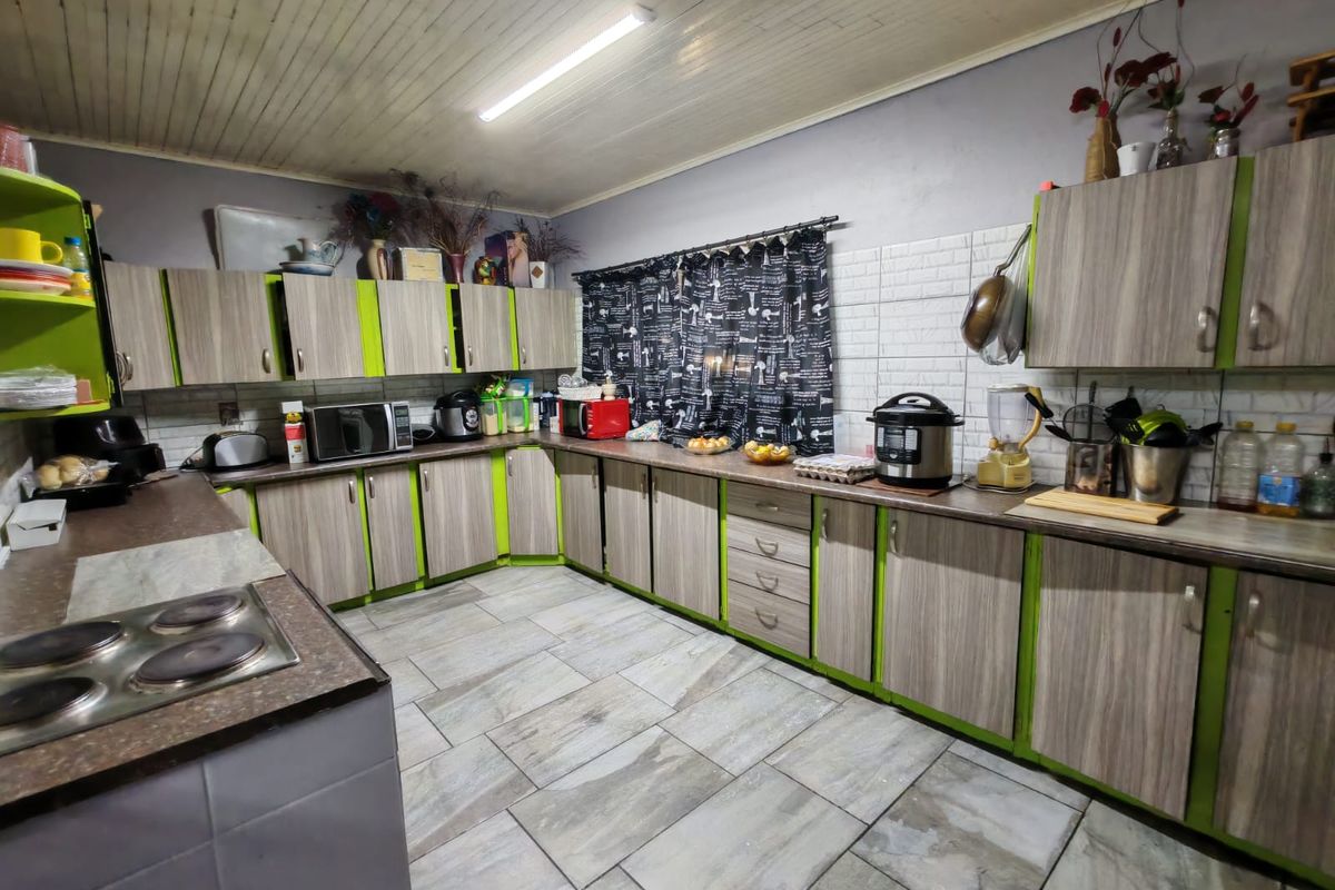A functional kitchen featuring extensive laminate cabinetry, a built-in electric hob, tiled backsplash, and durable floor tiles.