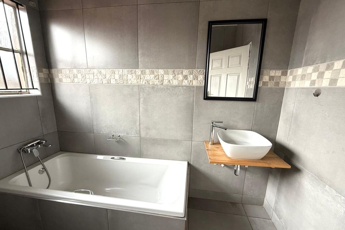 Modern bathroom featuring large format grey wall tiles, a built-in bathtub with chrome fixtures, and a vessel sink mounted on a timber vanity shelf.