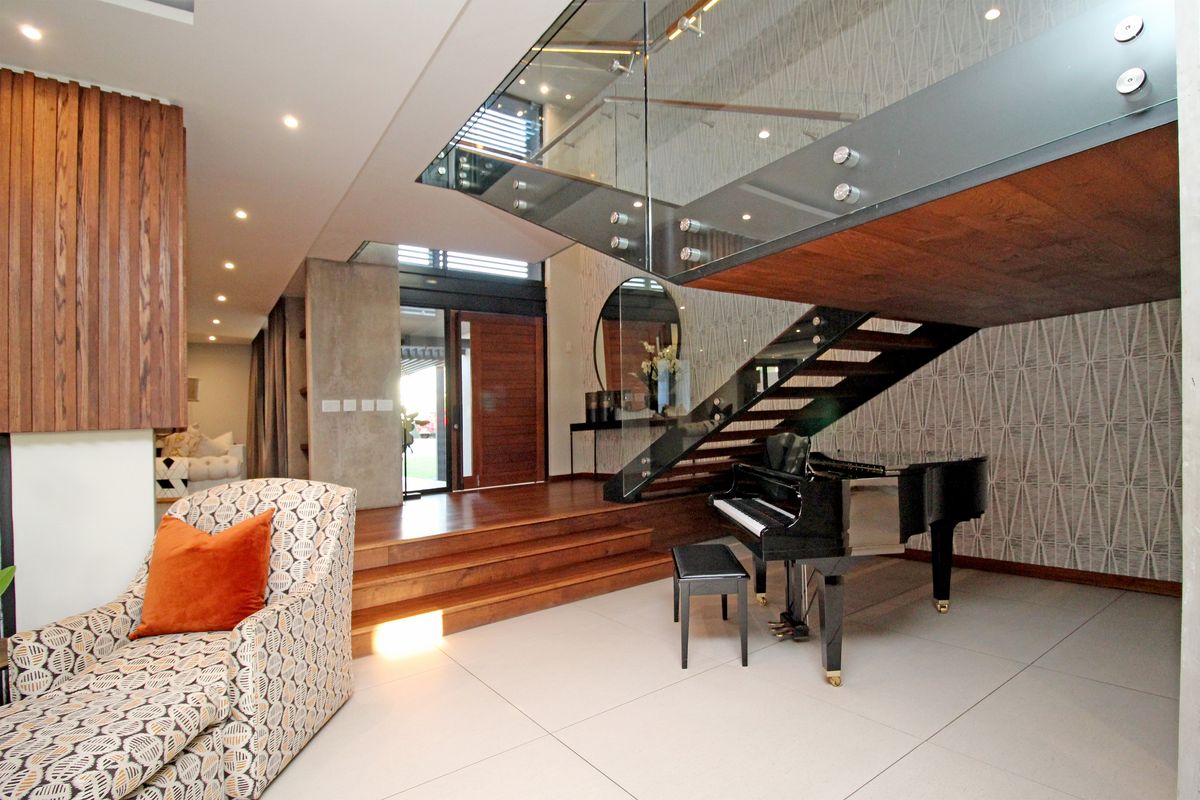 Modern open-plan living area featuring a striking floating staircase with glass balustrades, timber treads, and high-quality tiled flooring.