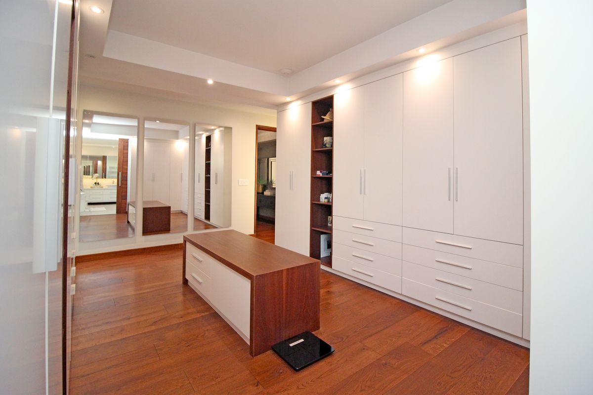 A spacious walk-in dressing room featuring extensive built-in cabinetry, integrated shelving, recessed ceiling lighting, and polished hardwood flooring.
