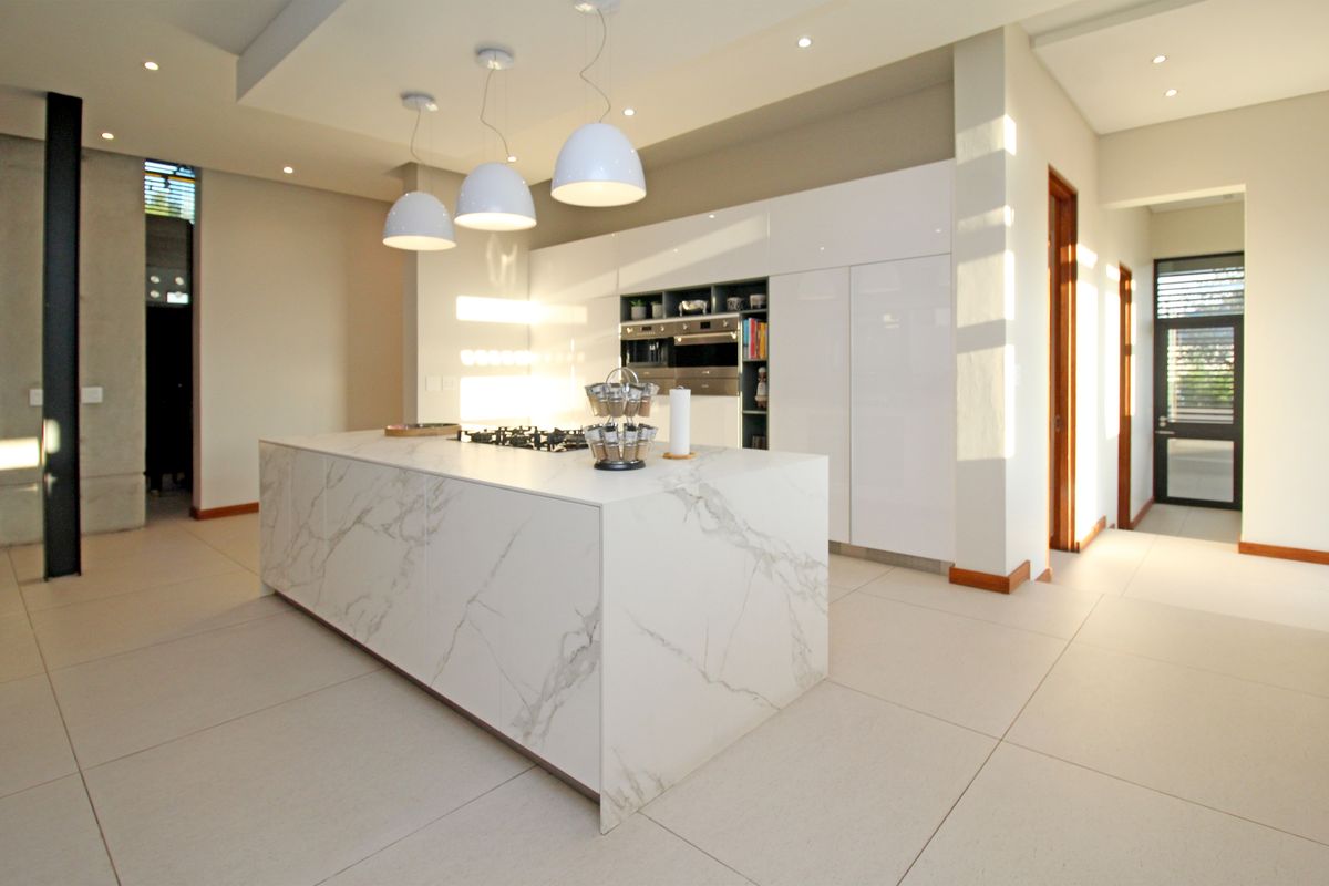 Modern open-plan kitchen featuring a large marble-topped island, sleek white cabinetry, integrated appliances, and recessed ceiling lighting.