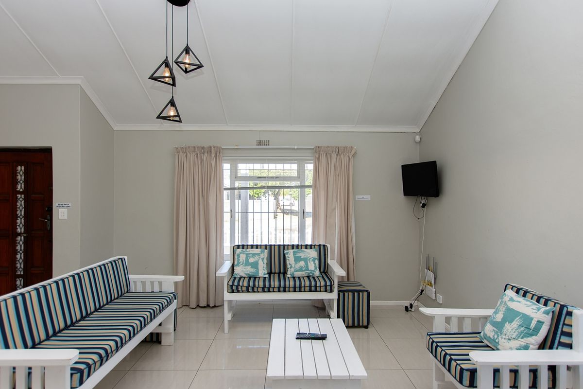 A bright living room featuring tiled flooring, a vaulted ceiling, and a window fitted with security bars.
