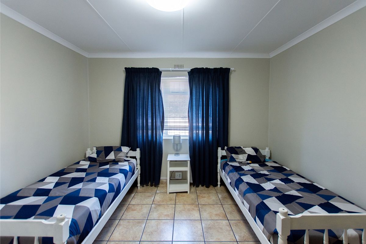 A functional bedroom featuring tiled flooring, neutral wall finishes, and a central window with fitted blinds.