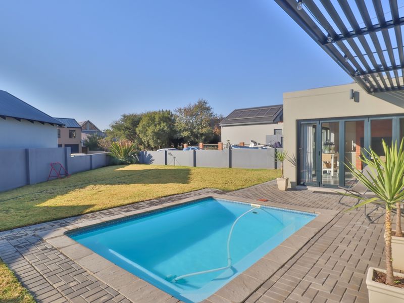 A well-maintained backyard featuring a swimming pool, paved patio area, modern pergola, and secure boundary walls, providing an ideal space for outdoor relaxation.