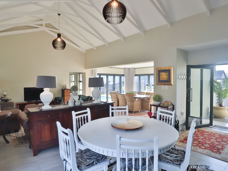 Spacious open-plan living and dining area featuring a high vaulted ceiling with exposed rafters, tiled flooring, and large bi-fold doors leading to the outdoors.