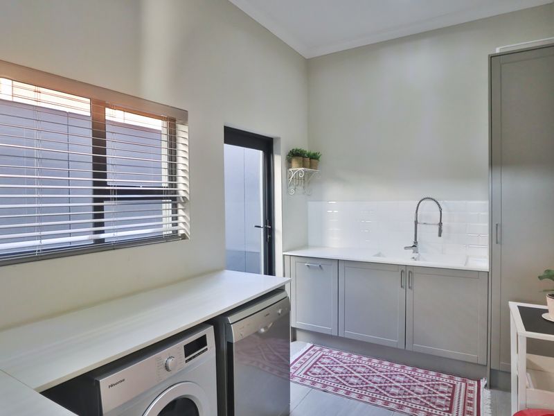 Modern laundry room featuring sleek grey cabinetry, subway tile backsplash, undermount sink with gooseneck faucet, and ample storage space.