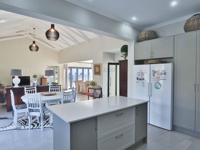 Spacious open-plan living area featuring a modern kitchen with a central island, vaulted ceilings with exposed rafters, and seamless flow to the dining space.