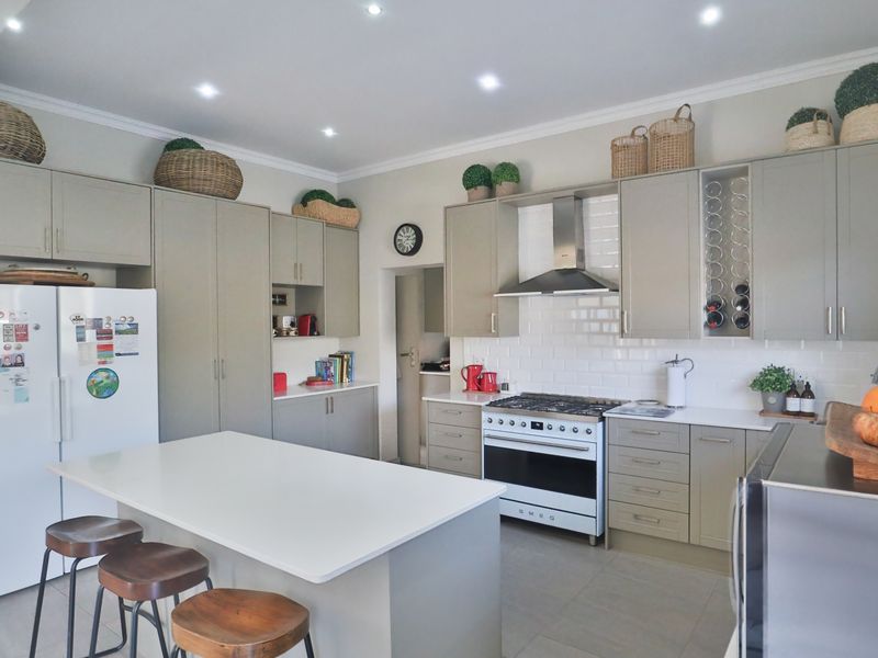 Modern kitchen featuring light grey cabinetry, a central island with seating, subway tile backsplash, and a professional-style gas range with extractor fan.