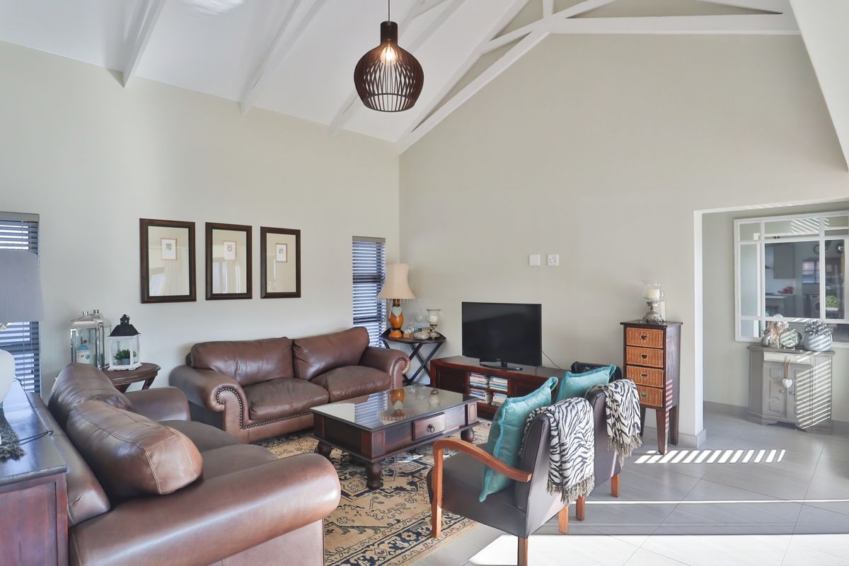 A spacious living room featuring a high vaulted ceiling with exposed rafters, neutral walls, and tiled flooring, offering a bright and airy atmosphere.