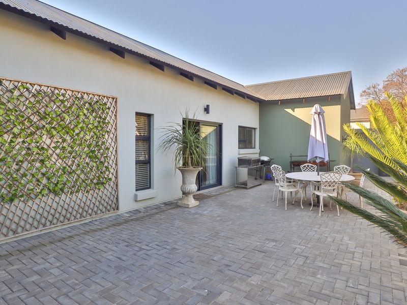 A well-maintained paved patio area featuring a sliding glass door entrance, corrugated metal roofing, and decorative trellis wall paneling.