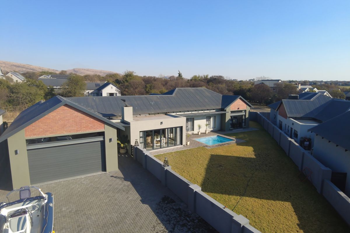 Aerial view of a modern residential property featuring a swimming pool, paved driveway, attached garage, and a well-maintained garden with boundary walls.
