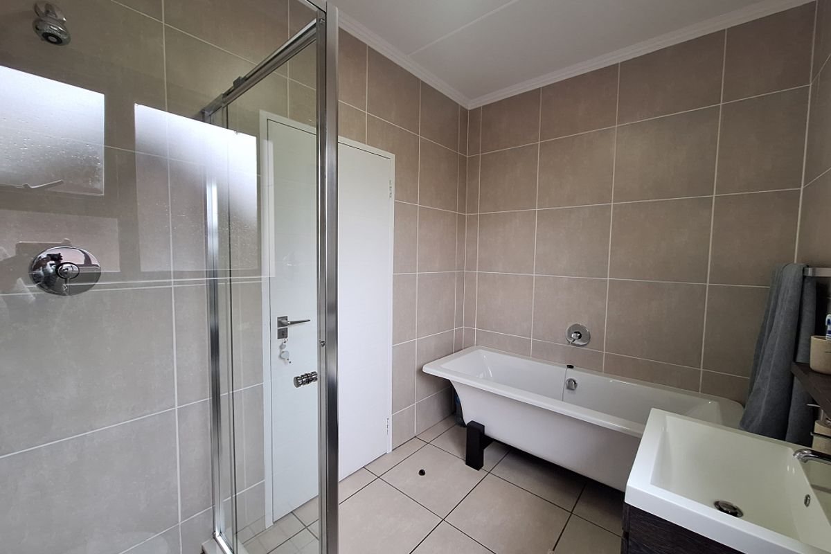 A modern bathroom featuring a glass-enclosed shower, a freestanding bathtub, and a vanity unit with neutral wall and floor tiling.