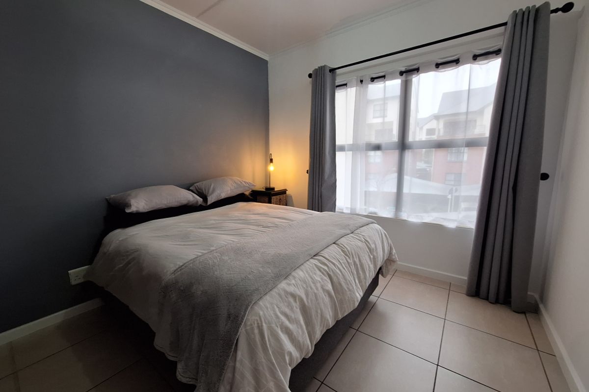 A well-lit bedroom featuring neutral tiled flooring, a dark accent wall, and large windows with fitted curtain rods.