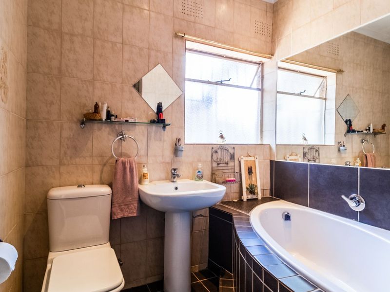 A functional bathroom featuring a pedestal basin, built-in bathtub, and tiled finishes, offering a classic layout with natural light from a casement window.