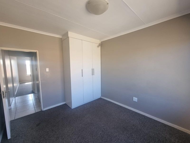 A clean, empty bedroom featuring neutral grey walls, fitted carpet flooring, and a built-in white wardrobe, offering a versatile space ready for personalization.