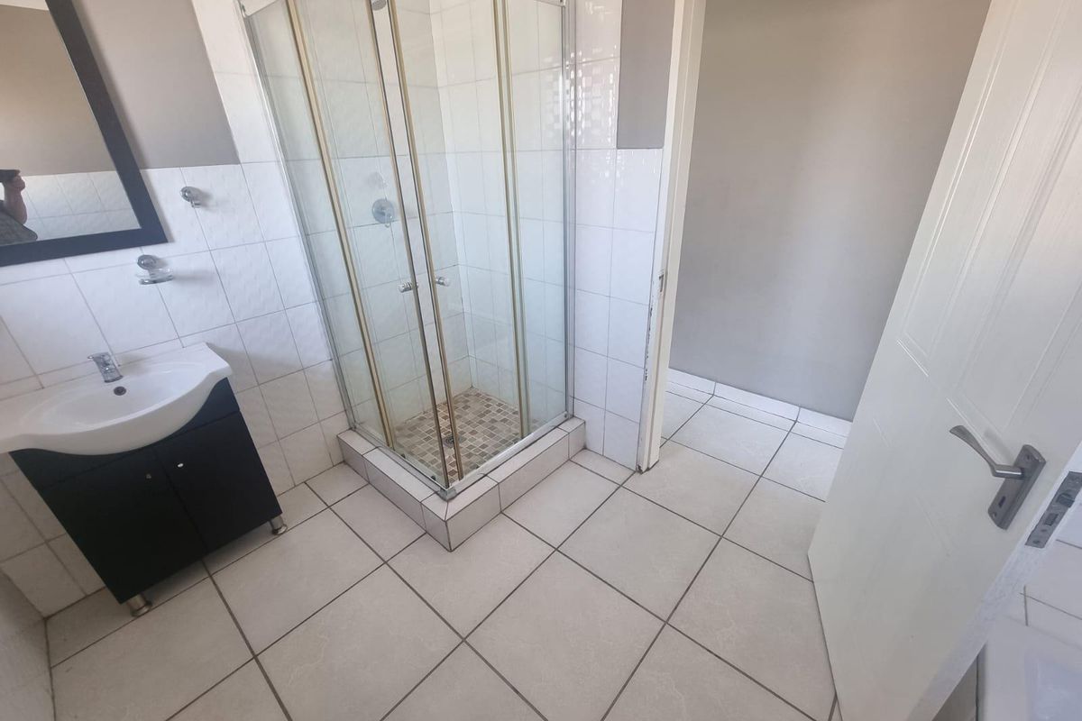 A functional bathroom featuring a corner shower enclosure, a vanity cabinet with a basin, and neutral tiled finishes.