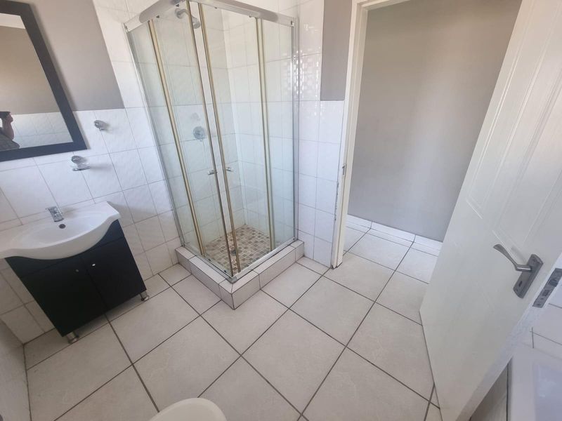 A functional bathroom featuring a corner shower enclosure, a vanity cabinet with a basin, and neutral tiled finishes.