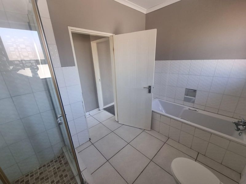 A functional bathroom featuring a built-in bathtub, separate shower enclosure, and neutral wall and floor tiling.