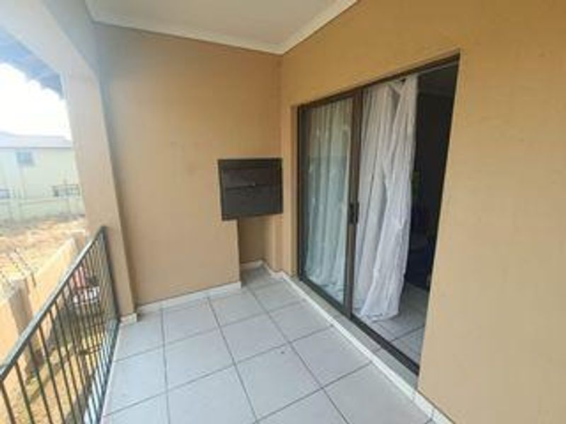 A covered balcony featuring tiled flooring, a built-in braai, and a sliding glass door providing access to the interior living space.