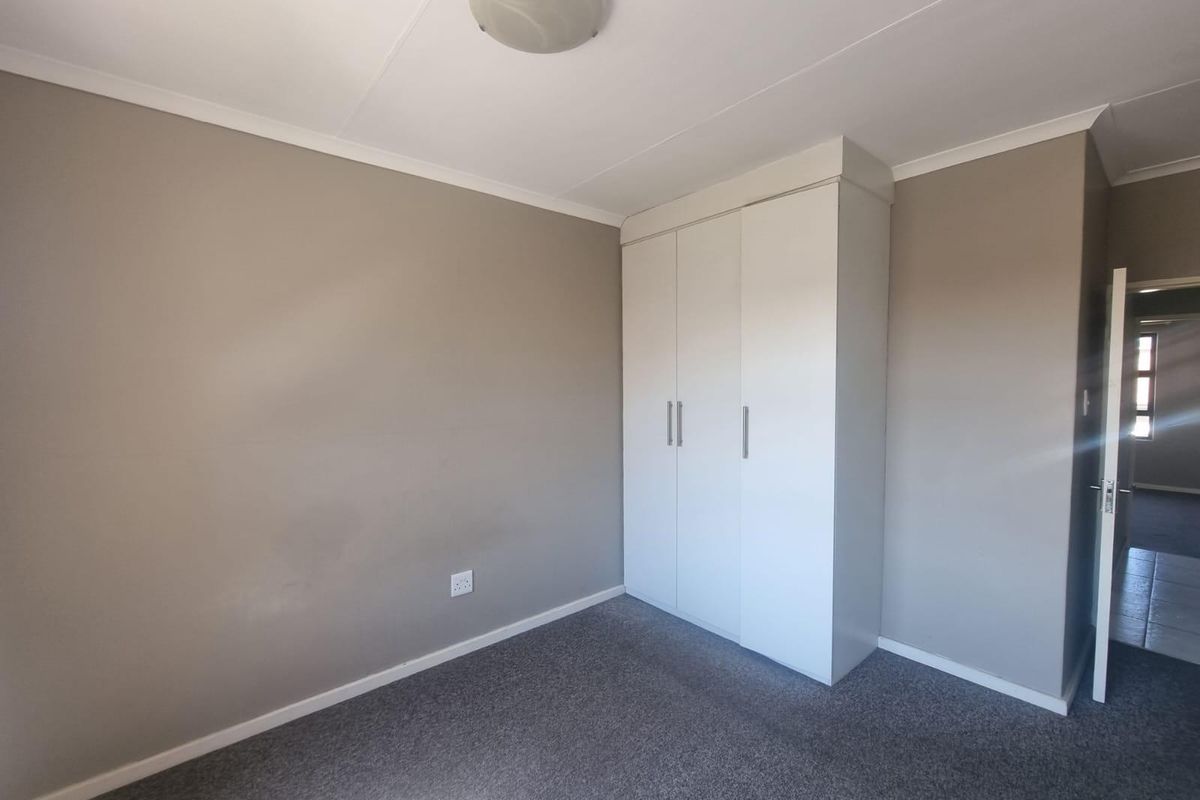 A clean, empty bedroom featuring neutral wall paint, grey carpeting, and a white built-in wardrobe with modern handles.