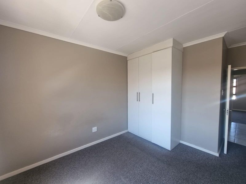 A clean, empty bedroom featuring neutral wall paint, grey carpeting, and a white built-in wardrobe with modern handles.