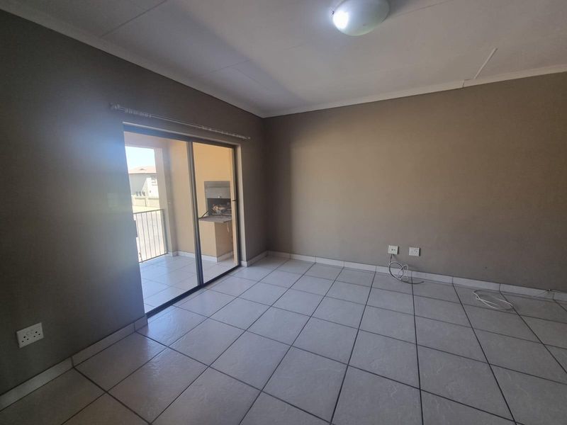 An empty living room featuring tiled flooring and a sliding glass door that opens onto a balcony with a built-in braai.