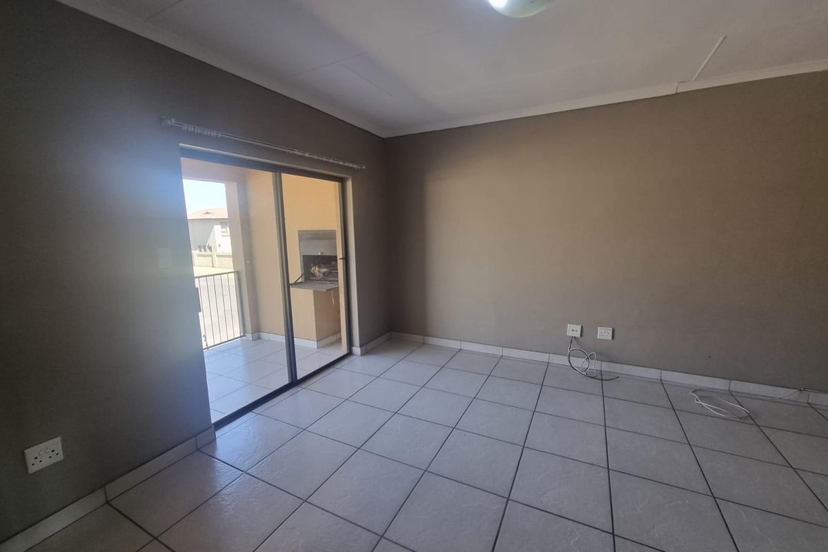 An empty living room featuring tiled flooring and a sliding glass door that opens onto a balcony with a built-in braai.