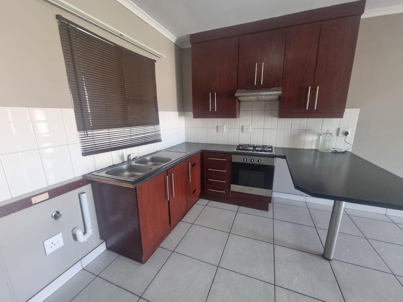 A functional kitchen featuring dark wood cabinetry, laminate countertops, a built-in oven with gas hob, and tiled flooring with a breakfast bar extension.