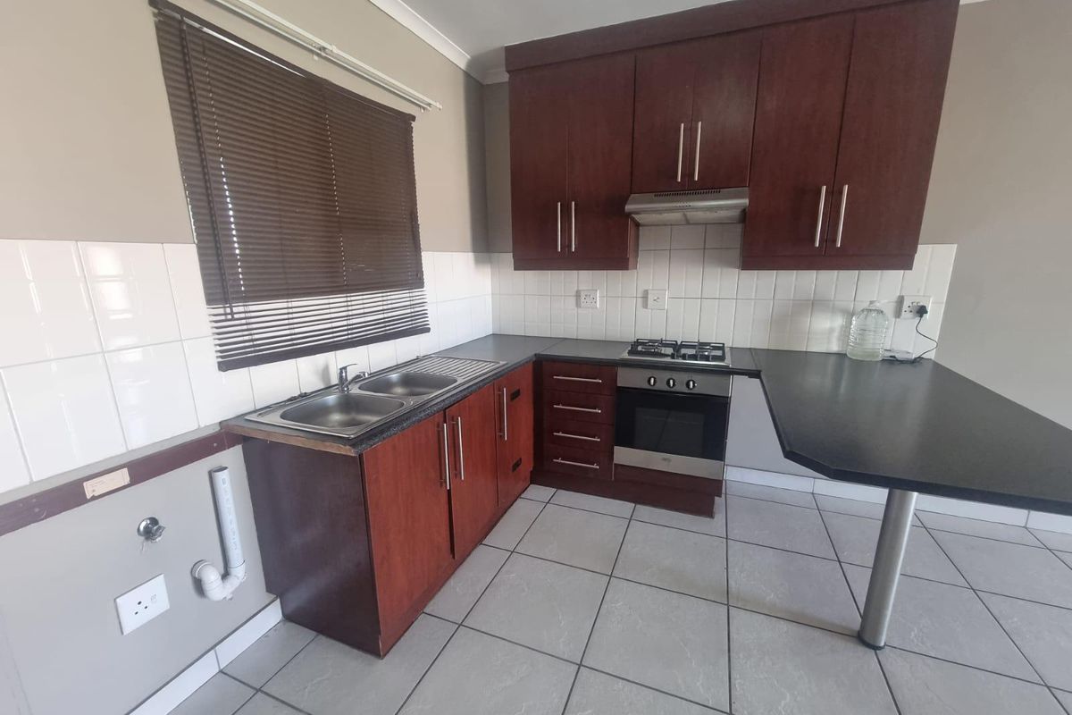 A functional kitchen featuring dark wood cabinetry, laminate countertops, a built-in oven with gas hob, and tiled flooring with a breakfast bar extension.